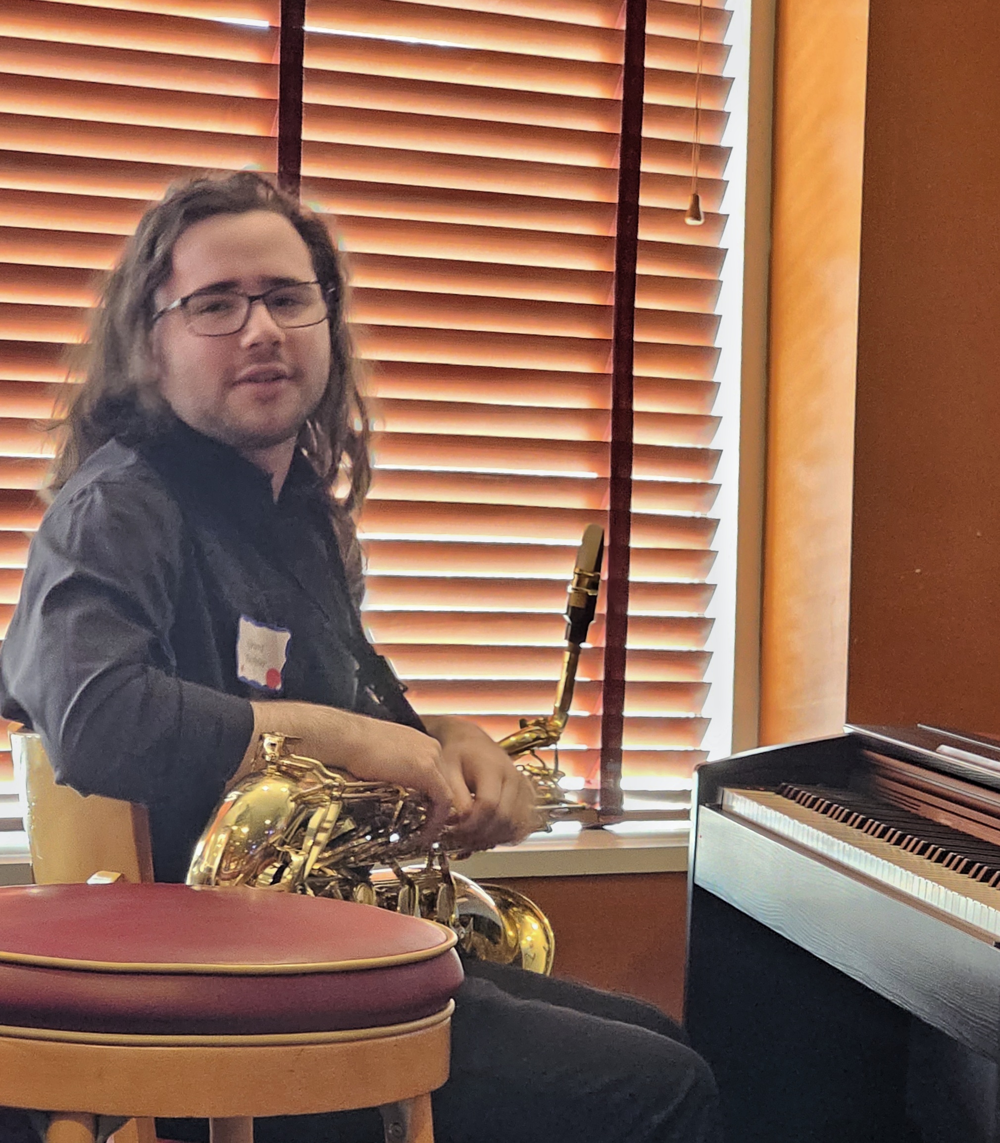 Grant Richter, a dark-haired teen, sits at a piano keyboard holding a baritone sax, preparing to perform his original music composition